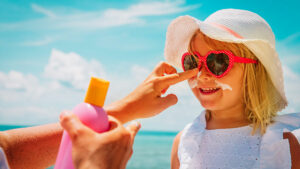 putting sunscreen on child wearing sunglasses and hat
